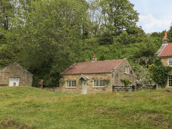 A stone cottage with a red-tiled roof, surrounded by lush greenery and trees. - Quoits Cottage, Goathland (Whitby)