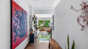 Een gang met een groot abstract schilderij, een houten bank en uitzicht op een balkon met planten.