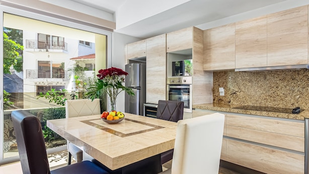Een moderne keuken met een marmeren aanrechtblad, inbouwapparatuur en een eethoek met een tafel en stoelen.