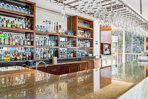 Een bar met drankflessen op planken, een gepolijst granieten aanrecht en een moderne kroonluchter.