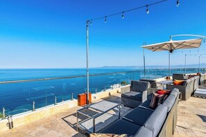 A rooftop terrace with outdoor seating, a glass balustrade, and a view of the sea. - Modern hillside suite with balcony, city view, pools, gym & full kitchen (Puerto Vallarta)
