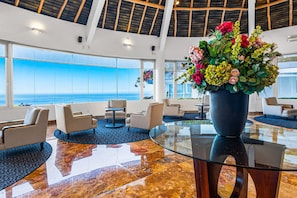 A lobby with a glass coffee table, seating area, and a large flower arrangement. - Well-located hillside suite with rooftop pool, fitness center & family features (Puerto Vallarta)