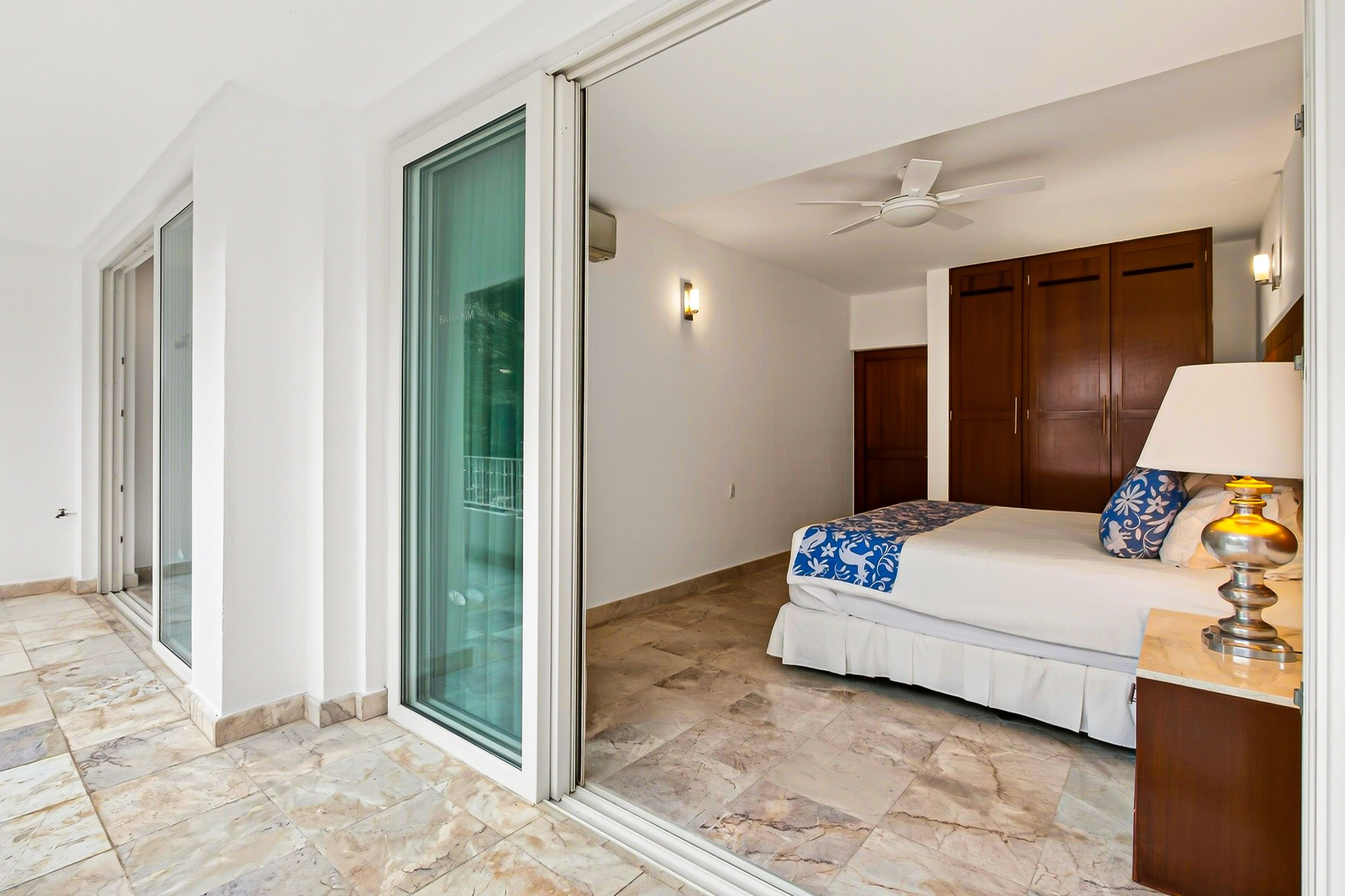 A bedroom with a bed, a ceiling fan, and a sliding glass door leading to a balcony.