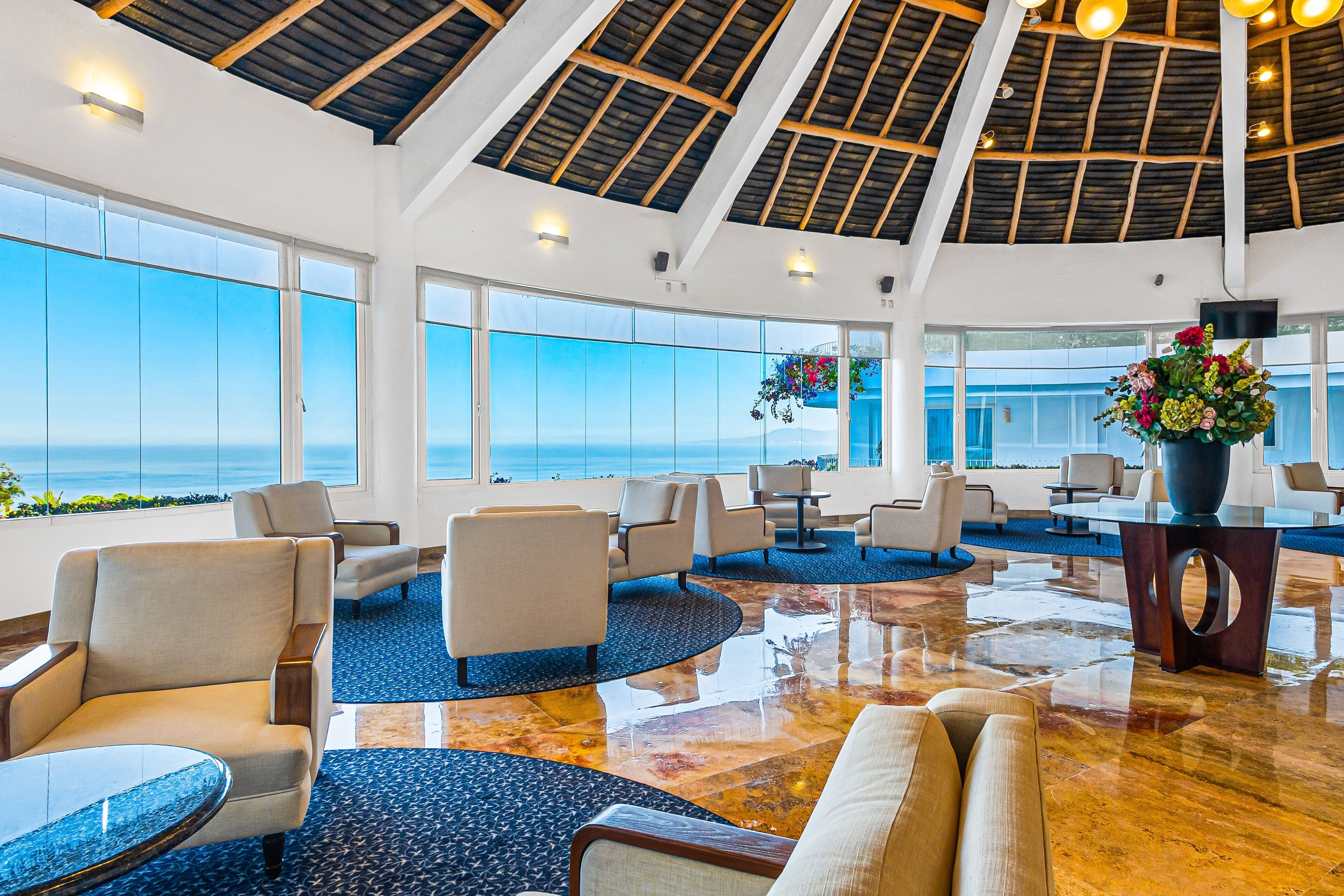 A spacious lobby with a high ceiling, large windows offering ocean views, and a variety of seating arrangements.
