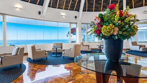 Eine großzügige Lobby mit einem großen Glastisch, bequemen Sitzgelegenheiten und Meerblick.