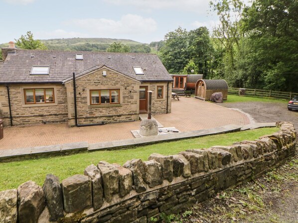 A stone building with a paved courtyard, a wooden fence, and a car parked outside.