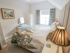 A hotel room with a bed, a bedside table, a lamp, a wardrobe, a television, and a window with curtains. - May Cottage, Snainton (Scarborough)