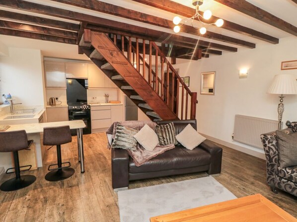 A living room with a staircase, a sofa, a coffee table, and a kitchen area.