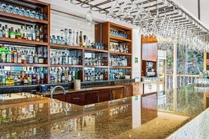 Un bar avec des étagères remplies de bouteilles d’alcool, un comptoir en granit poli et un lustre moderne.