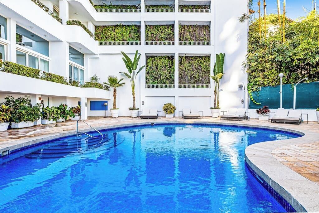 A swimming pool with a curved edge, surrounded by white walls and potted plants.
