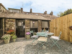 A stone building with a tiled roof, a wooden fence, a gravel patio, and outdoor seating with chairs and a table. - Poppy's Cottage Retreat in Grasmere (Ambleside)