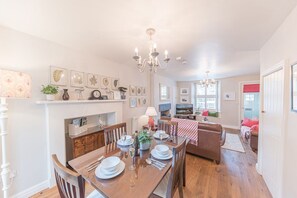 A dining area with a wooden table set for four, a chandelier, and a fireplace. - Poppy's Cottage Retreat in Grasmere (Ambleside)