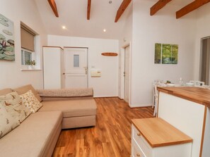 Un interior modern amb un sofà, terres de fusta, una cuina i una porta que dona a una altra habitació.