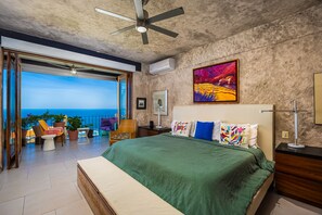 Une chambre à coucher avec un lit, un ventilateur de plafond, un tableau et une vue sur l’océan.