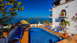 A pool area with lounge chairs, a thatched umbrella, and a view of the sea. - Paraiso del Mar 1BR/1BA Ocean View in Puerto Vallarta (Puerto Vallarta)