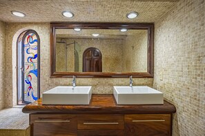 Une salle de bain avec deux lavabos, un grand miroir et une fenêtre à vitraux.