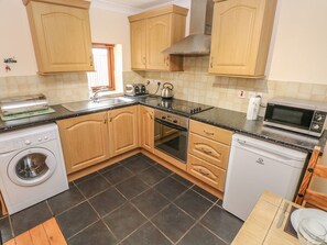 A kitchen with wooden cabinets, a washing machine, an oven, a microwave, and a sink. - The Stall, Llanmorlais (Swansea)