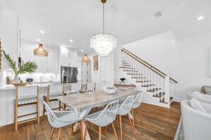 A modern kitchen with white cabinets, a wooden dining table, and a staircase.