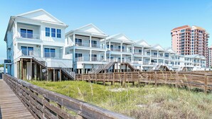 Ein Hotel direkt am Strand mit mehrstöckigen Gebäuden, einer Holzpromenade und einem strahlend blauen Himmel.