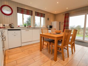 A kitchen with a dining table and chairs, a clock, and a window with a view. - Holly Lodge, Goosnargh (Preston)