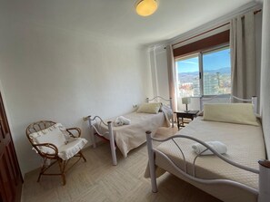 A bedroom with two beds, a chair, a small table, and a view of a cityscape. - Terrasol Madrid 9 in Torre del Mar (Velez-Malaga)