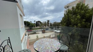 Ein Balkon mit rundem Tisch und zwei Stühlen, Blick auf eine Straße mit Autos und ein Gebäude mit weißer Fassade.