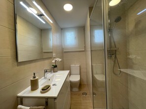 A modern bathroom with a large mirror, a sink, a toilet, and a glass-enclosed shower. - Terrasol LOS Angeles 2 (Velez-Malaga)