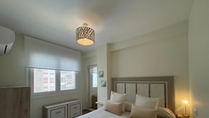 Ein Schlafzimmer mit Bett, Nachttischen, einem Fenster und einer Deckenleuchte.