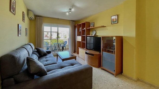A living room with a sofa, TV, and wooden cabinets. - Terrasol Zeus in Torre del Mar (Velez-Malaga)