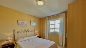 A bedroom with a bed, two bedside lamps, a window with curtains, and two wall-mounted paintings. - Terrasol Zeus in Torre del Mar (Velez-Malaga)