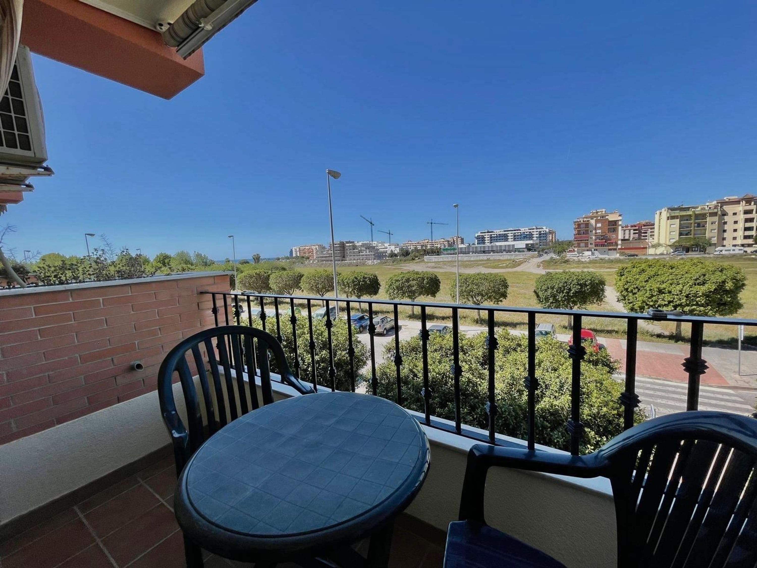 A balcony with a table and chairs, a view of a parking lot, and buildings in the background.