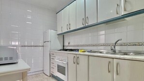 Een keuken met witte kastjes, een fornuis, een koelkast en een spoelbak.