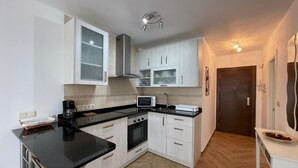 A compact kitchen with white cabinets, a black countertop, a microwave, a stove, and a small dining area with a chair and table. - Terrasol SAN Francisco Larios (Velez-Malaga)