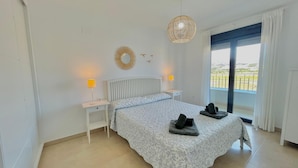 A bedroom with a bed, two bedside tables, a hanging light fixture, a window with a view, and a decorative mirror on the wall. - Terrasol Azucarera 4 (Velez-Malaga)