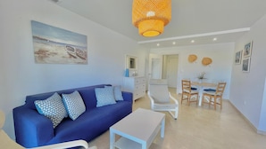 A living room with a blue sofa, a white coffee table, and a dining area with a table and chairs. - Terrasol Azucarera 4 (Velez-Malaga)