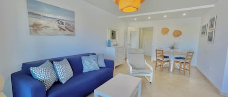 Un salon avec un canapé bleu, une table basse blanche et un coin repas comprenant une table et des chaises.