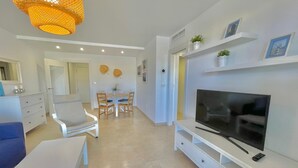 A modern living room with a TV, white furniture, a dining area, and a hanging light fixture. - Terrasol Azucarera 4 (Velez-Malaga)