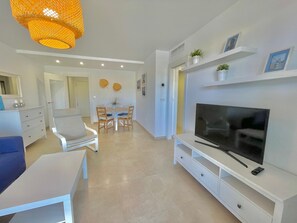 A modern living room with a TV, white furniture, a dining area, and a hanging light fixture. - Terrasol Azucarera 4 (Velez-Malaga)