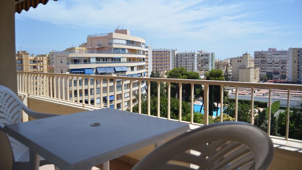 A balcony with a table and chairs, overlooking a cityscape with multiple buildings and a clear sky. - Terrasol Palma in Torre del Mar (Velez-Malaga)