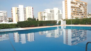 A swimming pool with a clear reflection of buildings, surrounded by greenery and a paved walkway. - Terrasol Palma in Torre del Mar (Velez-Malaga)
