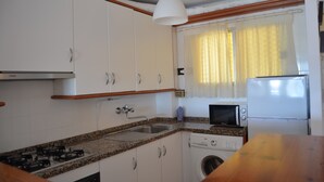 A compact kitchen with white cabinets, a gas stove, a washing machine, a microwave, and a refrigerator. - Terrasol Palma in Torre del Mar (Velez-Malaga)