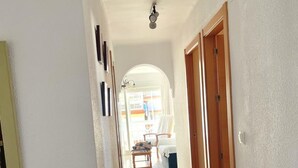 Ein Flur mit Fliesenboden, einer Holztür und einer weißen Wand mit einer Leuchte.
