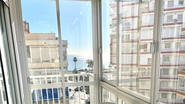 Ein Balkon mit weißem Tisch und Stuhl, großen Fenstern und Blick auf Gebäude sowie das Meer.