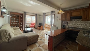 Een woonkamer met een bank, een eettafel en een keuken met kastjes en een aanrecht.
