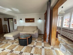 Ein Wohnzimmer mit einem Ecksofa, einem Glastisch und einem Musterparkettboden.