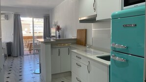 A modern kitchen with white cabinets, a turquoise SCHNEIDER refrigerator, and a tiled floor. - Terrasol Plazamar 6-2 (Velez-Malaga)