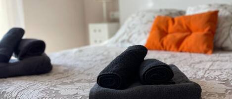 A neatly made bed with rolled towels and an orange pillow.