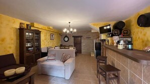 A living room with a sofa, a dining table, a kitchen area with a bar, and a clock on the wall. - Terrasol Moriles in Torre del Mar (Velez-Malaga)