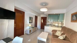 A living room with a sofa, a coffee table, a TV, and a kitchen area with cabinets and a countertop. - Terrasol California 4 (Velez-Malaga)