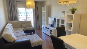 Una sala de estar con un sofá modular, una mesa de comedor, un televisor y una estantería.